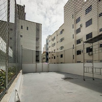 Quadra esportiva cercada com estrutura em inox, tela alambrado nas laterais e rede de proteção no teto.