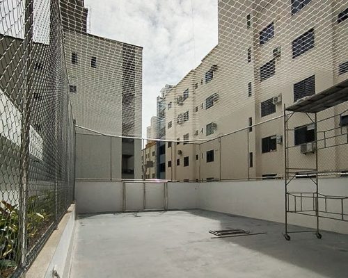Quadra esportiva cercada com estrutura em inox, tela alambrado nas laterais e rede de proteção no teto.