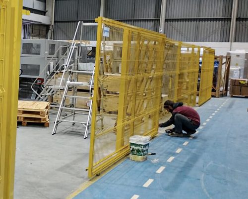 Cercamento em gradil metálico amarelo instalado em área industrial para proteção e isolamento de máquinas.
